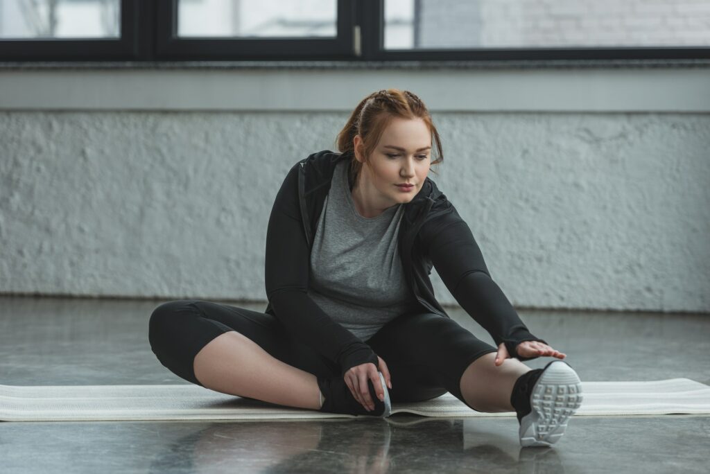 Obese girl stretching on floor in gym